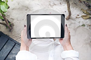 Mockup image of a woman`s hand holding black tablet pc with blank white desktop screen with sand and beach