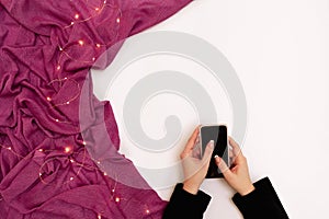 Mockup image of woman`s hand holding mobile phone with blank screen on white background with scarf in modern cafe