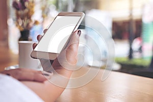 Mockup image of a woman`s hand holding white mobile phone with blank desktop screen and coffee cup