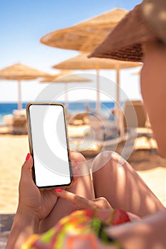 Mockup image of a woman`s hand holding white mobile phone with blank desktop screen by the sea and Beach resort background. woman