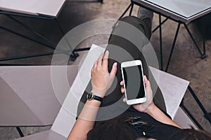 Woman`s hands holding white mobile phone with blank black screen on thigh in modern loft cafe