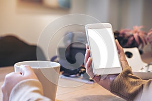 Mockup image of woman`s hands holding white mobile phone with blank screen on vintage wood table