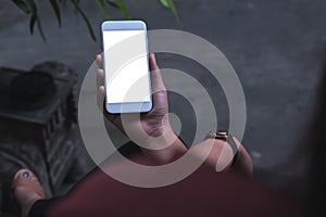 Mockup image of a woman sitting crossed leg and holding white mobile phone with blank screen with concrete floor