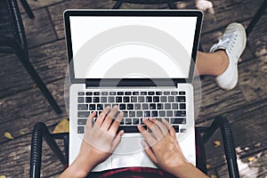 Mockup image of a woman sitting , using and typing on laptop with blank white screen on thigh at outdoor