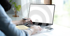 Mockup image of a woman using laptop with blank white screen on wooden table in office