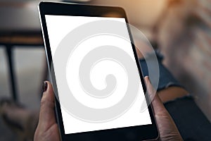 Mockup image of a woman wearing ripped jean sitting cross legged , holding black tablet pc with blank white desktop screen