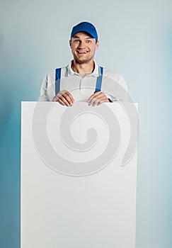 Mockup image of a young high smiling worker holding empty white banner. White or blue background. Bussines concept