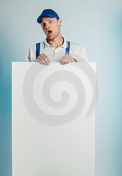 Mockup image of a young indignant worker holding empty white banner. White or blue background. Bussines concept