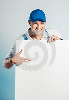 Mockup image of a young smiling worker holding empty white banner and points to it