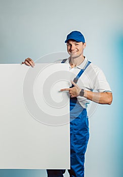 Mockup image of a young smiling worker holding empty white banner and points to it