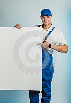 Mockup image of a young smiling worker holding empty white banner and points to it