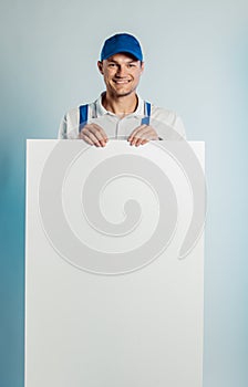 Mockup image of a young smilling worker holding empty white banner. White or blue background. Bussines concept