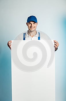 Mockup image of a young smilling worker holding empty white banner. White or blue background. Bussines concept