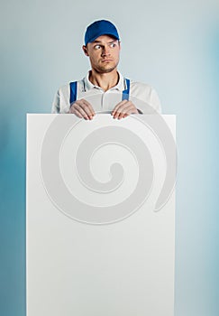 Mockup image of a young surprised worker holding empty white banner. White or blue background. Bussines concept