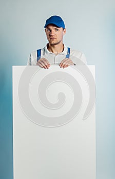 Mockup image of a young surprised worker holding empty white banner. White or blue background. Bussines concept