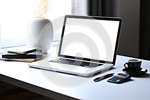 Laptop computer with empty screen, calculator and coffee cup on white table.