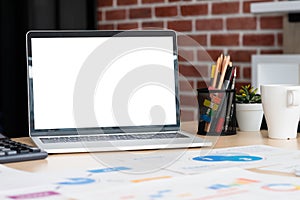 Mockup laptop computer screen with business chart market,caculator,coffee cup,pencil box on desk at brick wall at modern office