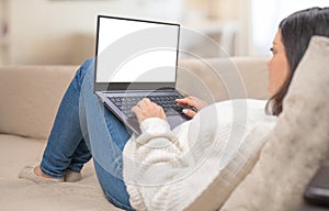 Mockup laptop. Woman looking at mock up blank white screen lying on sofa at home. woman using, working on laptop with blank screen