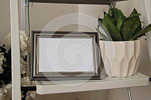 The mockup of the metallic photo frame and flower pot stand on the shelf