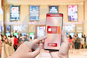 Mockup mobile phone hand using smartphone to buy cinema tickets with blurred image of ticket sales counter at movie theater with