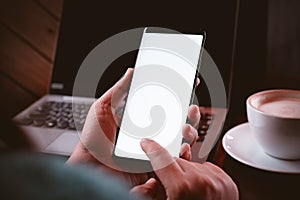 Mockup mobile phone image. Close up hands using modern smart phone Technology in coffee shop with blurred laptop and a cup of