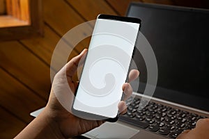 Mockup mobile phone image. Close up hands using modern smart phone Technology with blurred laptop background. Mobile phone with