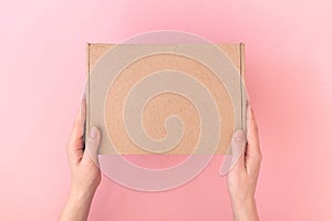 Mockup parcel cardboard box in a delivery woman man hands on a pink pastel background, table, delivery service concept