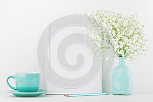 Mockup of picture frame decorated flowers in vase and coffee cup on white table with clean space for text and design your blogging