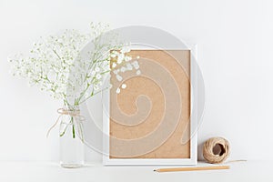 Mockup of picture frame decorated gypsophila flowers in vase on white working table with clean space for text and design your blog