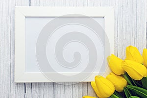 Mockup of picture frame decorated yellow tulip flowers on wooden background. Styled stock photography