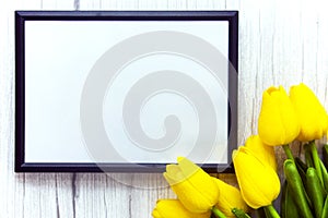 Mockup of picture frame decorated yellow tulip flowers on wooden background. Styled stock photography