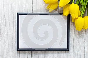 Mockup of picture frame decorated yellow tulip flowers on wooden background. Styled stock photography