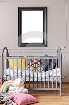 Mockup poster in black frame on the grey wall of baby room interior with crib with pillows, vertical view