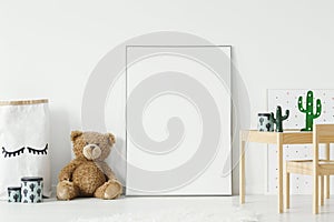 Mockup poster, teddy bear and material basket placed on the floor in white room interior with wooden table and small chair. Paste