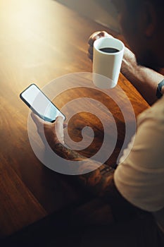 Mockup shot of man`s hand with tattoos holding  cell phone and coffee cup with blank screen on desk at home office