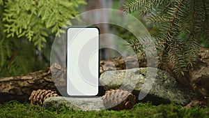 Mockup smartphone with blank screen on podium in green coniferous forest. Advertising of mobile apps for meditations