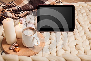 Mockup tablet with Cup of cappuccino and cookies, candles, checkered plaid on the background of blanket of thick yarn