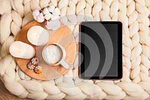 Mockup tablet with Cup of cappuccino and cookies, candles, checkered plaid on the background of blanket of thick yarn