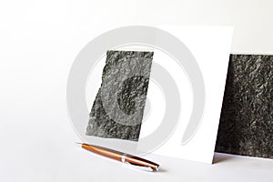 Mockup template with blank card standing next to black large stone with orange metallic parker pen