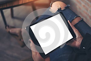 Mockup top view image of a woman wearing ripped jean sitting cross legged , holding black tablet pc with blank white desktop scree