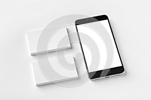 Mockup of two blank horizontal business cards and black cell-phone at white textured paper