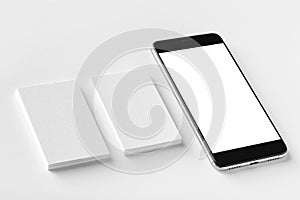 Mockup of two blank vertical business cards and black cell-phone at white textured paper.