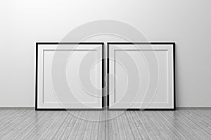 Mockup of two square frames with thin black frame border standing next to wall on wooden floor