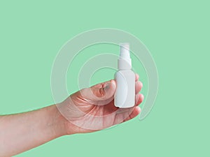 Mockup of unbranded white plastic spray bottle for branding and label and male hand on a green background. Liquid antimicrobial