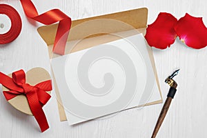 Mockup Valentines Day greeting card letter in envelope with kraft gift box red ribbon, flat lay on a white wooden