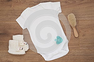 Mockup of white baby bodysuit on wood background with knitted booties. Blank baby clothes template mock up