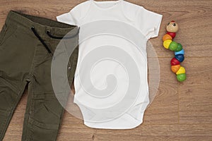 Mockup of white baby bodysuit on wood background with pants and colorful toy. Blank baby clothes template mock up, flat lay styled