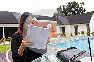 Mockup of a white blank hardcover book featuring a woman reading it near a pool