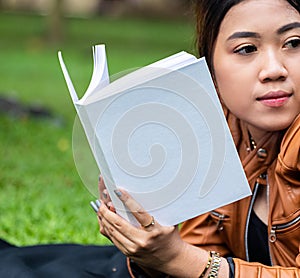 Mockup of a white blank hardcover book featuring a woman reading it at a park