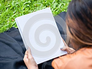 Mockup of a white blank hardcover book featuring a woman reading it at a park